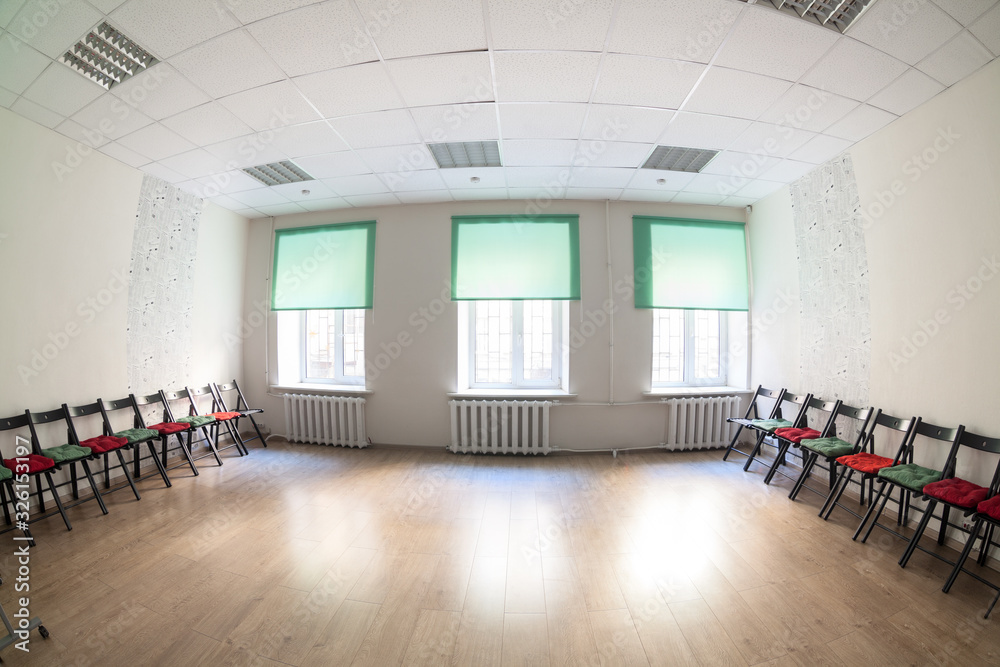 Fototapeta premium Large hall with three windows interior. Chairs along two sides, hardwood floor, beige walls and green curtains.