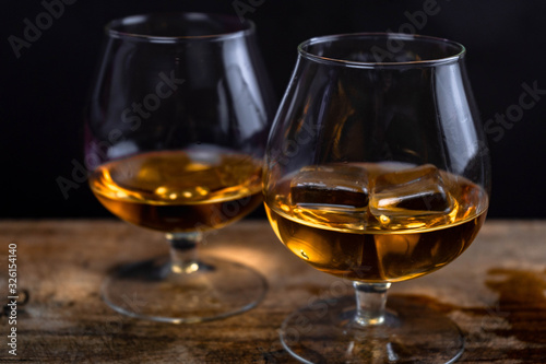 Two whiskey / cognac glasses with ice on a wooden background. Dark backdrop. © Zkolra