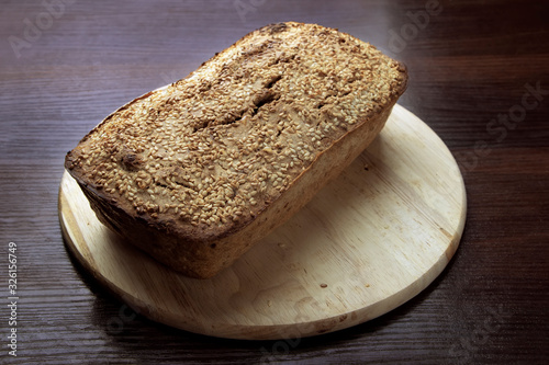 Freshly baked buckwheat bread. A loaf of bread lies on a round kitchen board on a brown wooden table. Gluten-free healthy home-made product. Natural nutrition for vegans and vegetarians