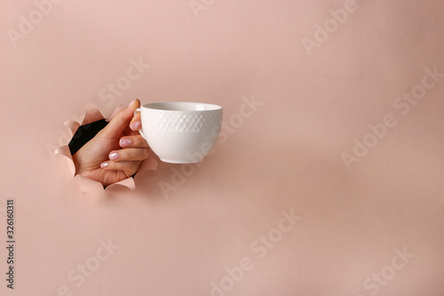 White cup in a female hand through round hole in pink paper, Coffee time, Copy space