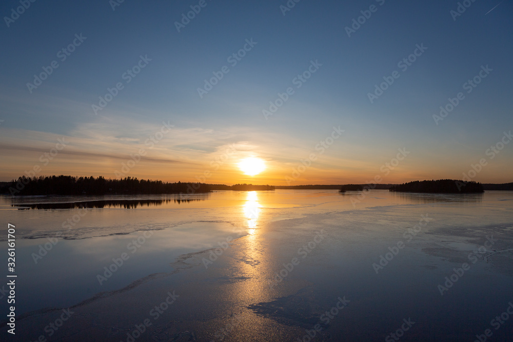 Amazing winter sunset in Finland. Cold afternoon in February, reflecting water and icy surface. Wintry landscape wallpaper, copy space.
