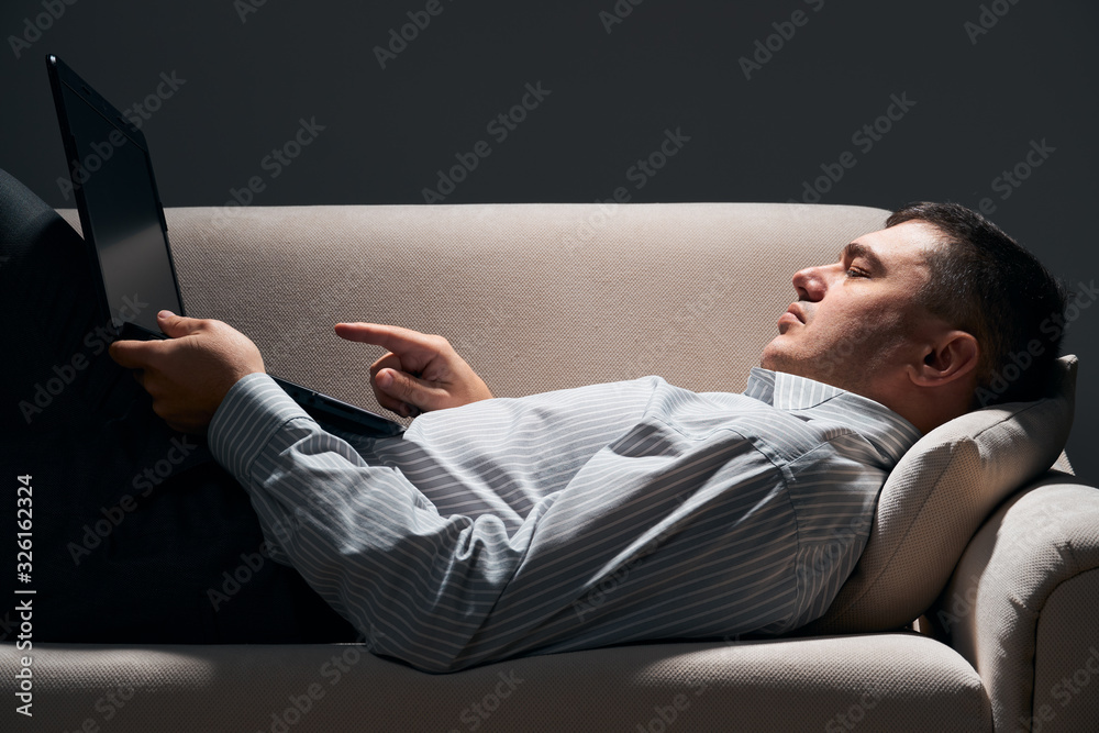 businessman is lying on the sofa and working with laptop