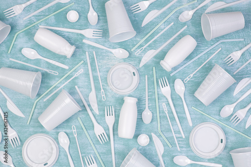 Disposable white single use plastic objects such as bottles, cups, forks and spoons on blue background