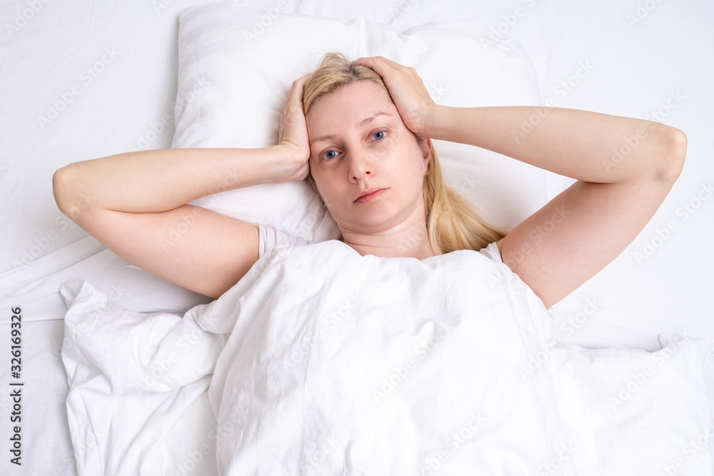 A beautiful sick woman lying in bed with a headache, migraine and suffering A beautiful sick woman lying in bed with a headache, migraine and suffering