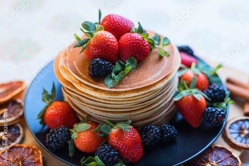 Homemade pancakes, fresh summer dessert with strawberries and blueberries on a black plate, close-up, selective focus. Still life with sweet dessert.