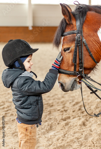 boy stroking horse, young jockey, horseback training on manege, lesson for young jockey in equestrian school or club, pet animal © Stockgurulab