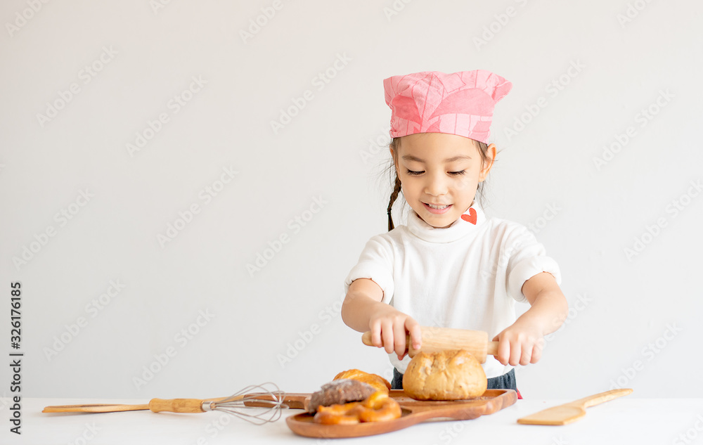 Asian little chef girl use rolling pin to play with bread and look fun on white background. Asian little chef girl use rolling pin to play with bread and look fun on white background.