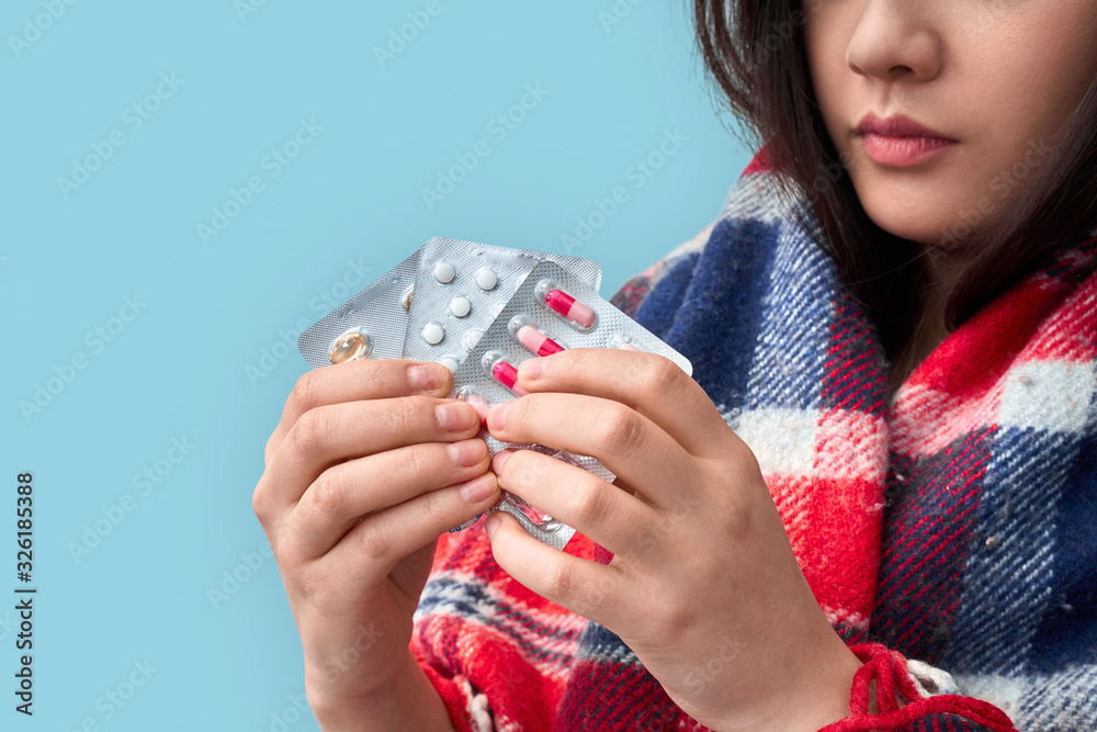 Influenza Concept. Chinese woman in plaid blanket standing isolated on grey holding pills blisters close-up concerned Influenza Concept. Chinese woman in plaid blanket standing isolated on grey holding pills blisters close-up concerned