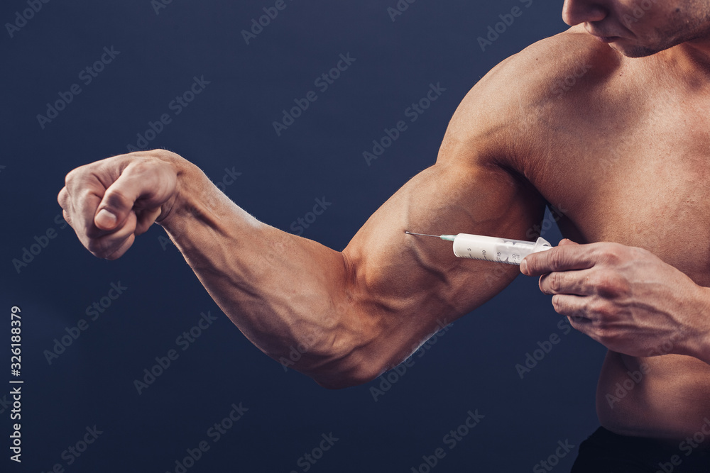 Bodybuilder makes injection of vitamins. Photo of sporty man with perfect physique on dark
