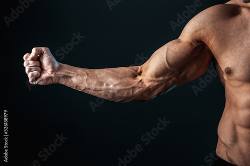 Fotografiet tense arm clenched into fist, veins, bodybuilder muscles on a dark background, isolate