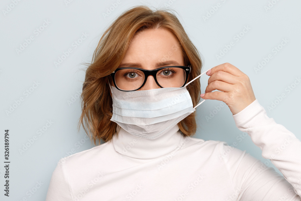 Studio portrait of woman in glasses wearing face medical mask, looking at camera, isolated on blue background, close up. Flu epidemic, dust allergy, protection against virus. Covid-19, coronavirus. Studio portrait of woman in glasses wearing face medical mask, looking at camera, isolated on blue background, close up. Flu epidemic, dust allergy, protection against virus. Covid-19, coronavirus.