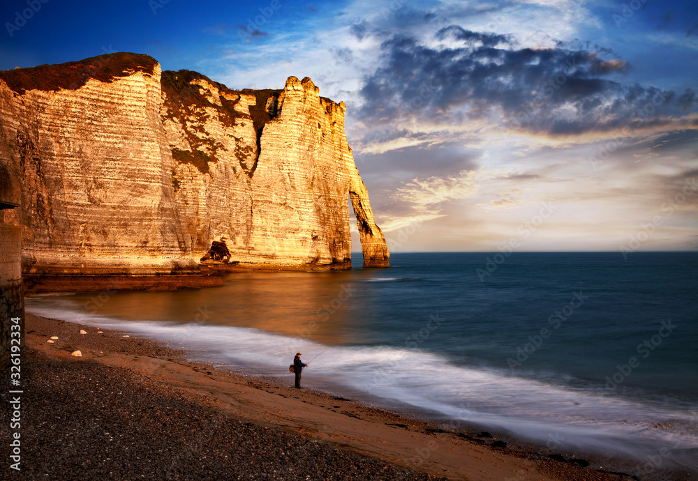 fisherman at sunrise on coastal landscape along the Falaise d'Aval the famous white cliffs of Etretat village with the Porte d'Aval natural arch and the rock known as the Aiguille d'Etretat fisherman at sunrise on coastal landscape along the Falaise d'Aval the famous white cliffs of Etretat village with the Porte d'Aval natural arch and the rock known as the Aiguille d'Etretat