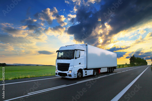 White truck driving through autumn landscape at sunset photo