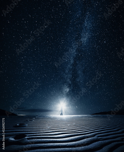 Man with flashlight walks in the sand at night under milky way
