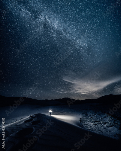 Man with flashlight walks in the sand at night under milky way