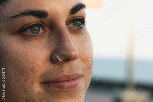 Nostalgic look of young woman with green eyes and piercing earring on nose. Girl portrait with lifeless gaze. Thoughtful expression concept