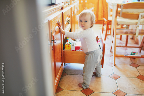 Adorable toddler girl at home, opening the drawer in the kitchen photo