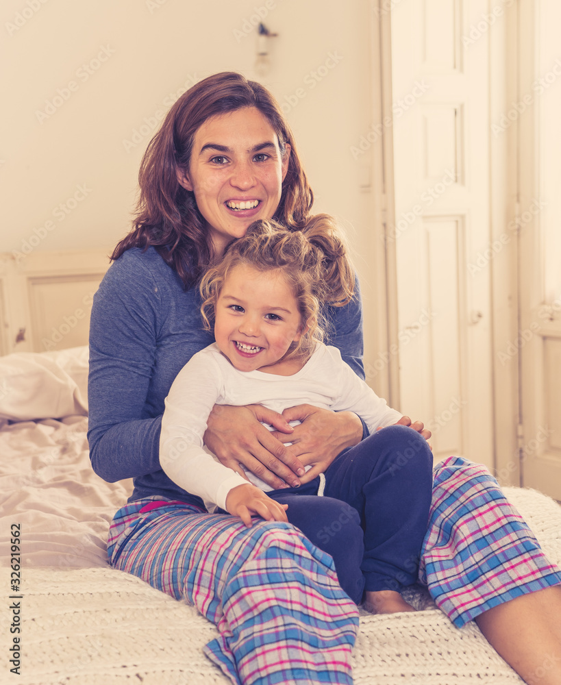 Lifestyle portrait of beautiful mother and daughter relaxing in bed. Mum and cute toddler girl having fun, kissing and hugging at home. Happy family, education and single parent concept. Lifestyle portrait of beautiful mother and daughter relaxing in bed. Mum and cute toddler girl having fun, kissing and hugging at home. Happy family, education and single parent concept.