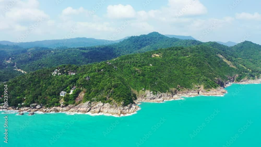 Paradise tropical island with beautiful hills covered in green vegetation, rocky coastline caved by turquoise lagoon under bright cloudy sky in Thailand Paradise tropical island with beautiful hills covered in green vegetation, rocky coastline caved by turquoise lagoon under bright cloudy sky in Thailand