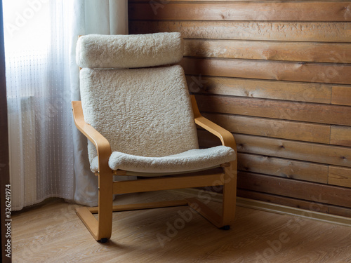 A comfortable chair in the corner near the window. Wooden walls. Cozy interior. Beautiful stylish alpine style room