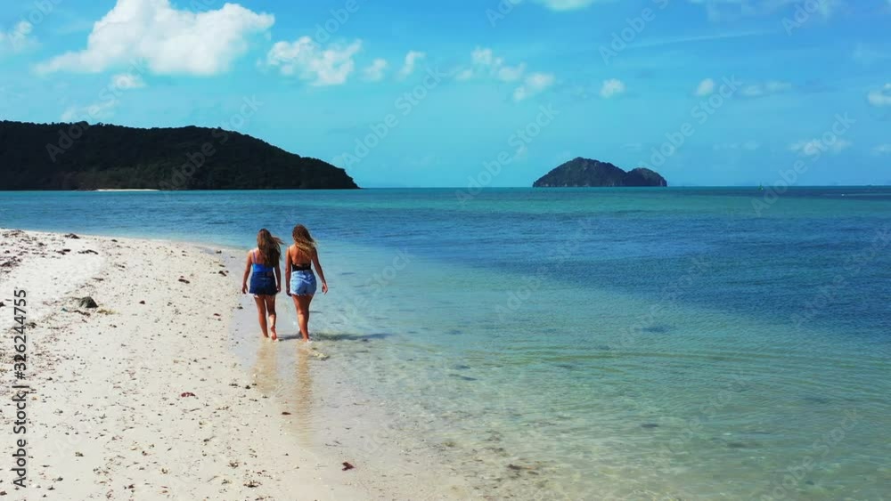 Young women walking on sandy exotic beach washed by calm clear water of shallow lagoon near resort on tropical island. Young women walking on sandy exotic beach washed by calm clear water of shallow lagoon near resort on tropical island.