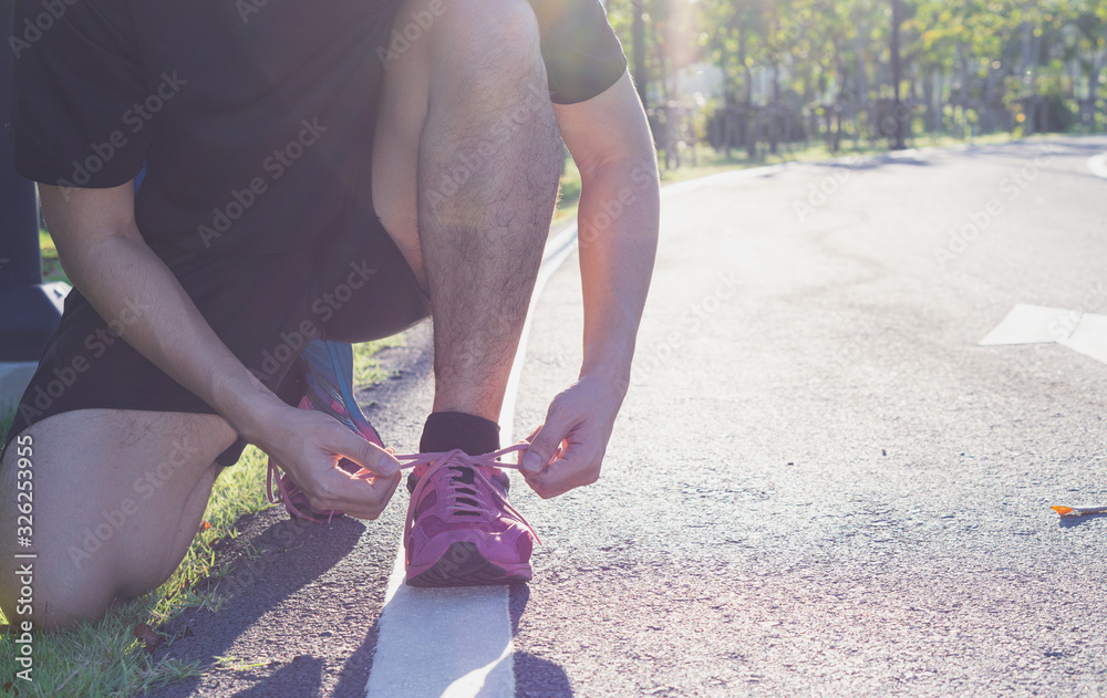 The male athlete is tying running shoe laces in the park with sunlight prepare for jogging in the garden. Sport and exercise concept.