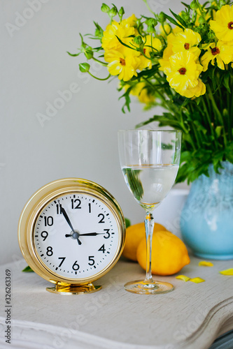 Golden clock on white background with lemons, flowers and glass of water