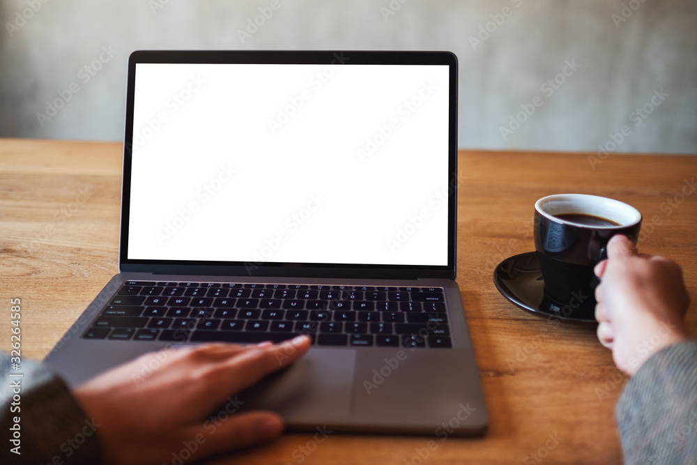 Mockup image of a woman using and touching on laptop computer touchpad with blank white desktop screen while drinking coffee Mockup image of a woman using and touching on laptop computer touchpad with blank white desktop screen while drinking coffee