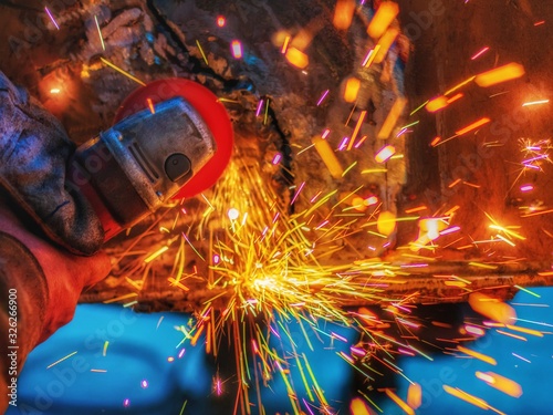 worker grinding cutting metal sheet with grinder machine overwrites the master of welding seams angle grinder and sparks. Electric grinder in the industrial workshop. photo