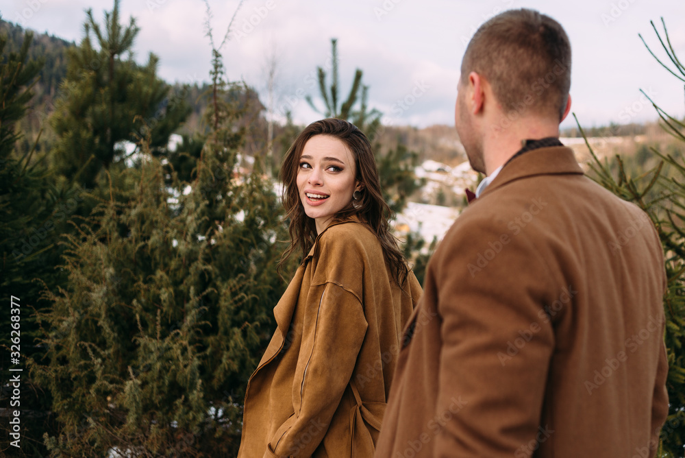 beautiful bride looks back at the groom on the background of coniferous bushes.
