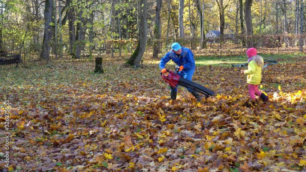 Happy family man and child playing together with leaf blower in autumn garden Happy family man and child playing together with leaf blower in autumn garden