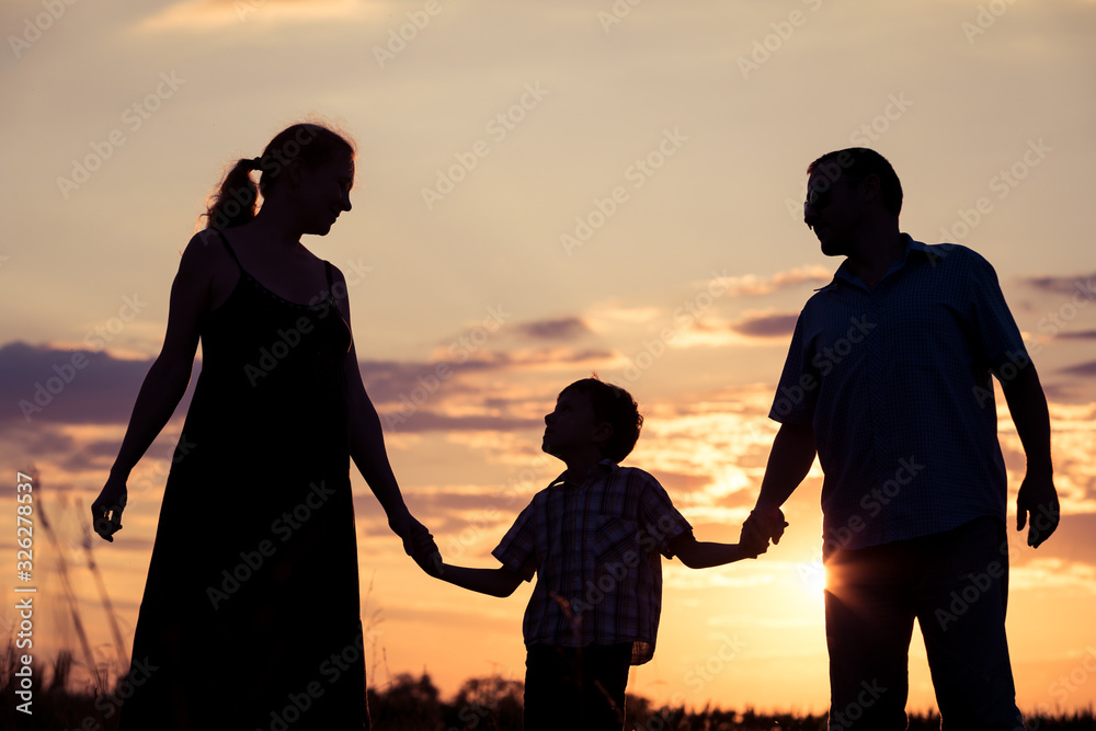 Happy family standing in the park at the sunset time.