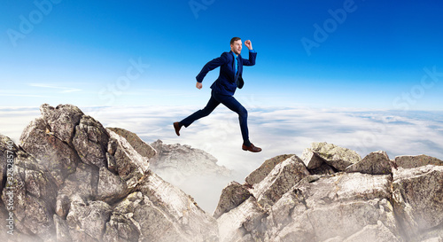 Businessman jumping through the gap among mountains.