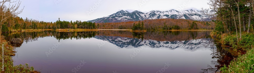 Beautiful lake reflecting blue sky like a mirror, rolling mountain range and woodland in the background on springtime sunny day. High latitude country natural beauty scenery