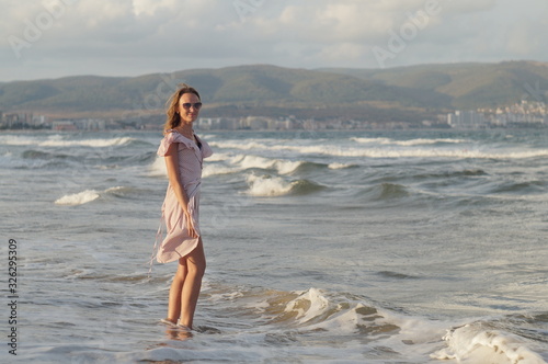 Young girl on the sea beach in a dress, evening wave and wind light, joyful mood.