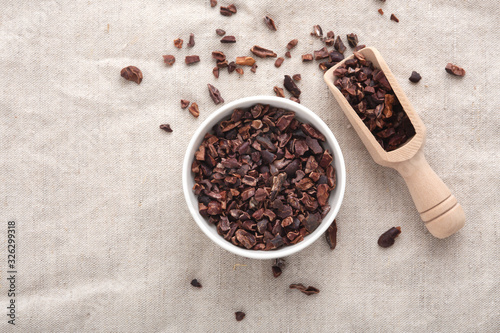 Cacao nibs in white bowl with wooden scoop