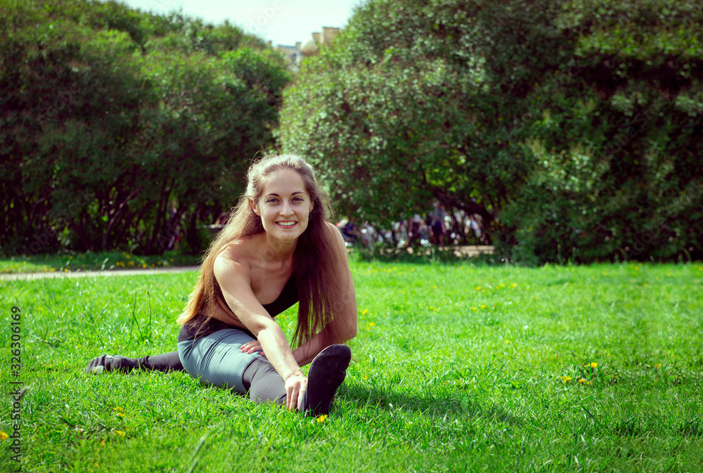 white young woman in sportswear with long hair doing a stretch on the grass in the Park