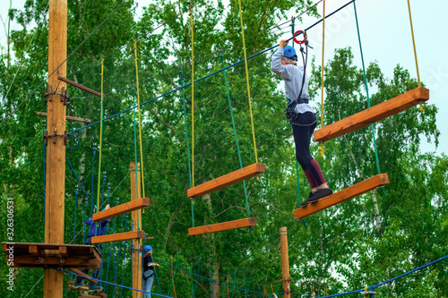 Children in the park in the attraction on the ropes with a safety rope, outdoor activities
