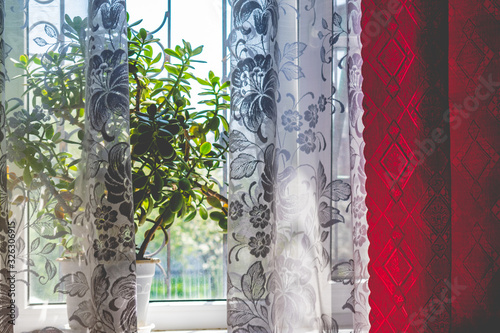 Home large and cozy window from which bright light passes into the room. Apartment fabric interior. Colored and transparent curtains with openwork pattern.