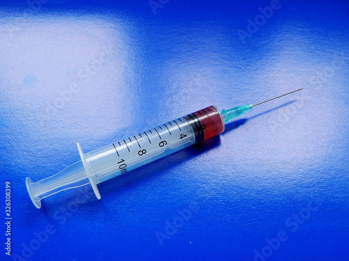 Syringe with medicine and needle, on a blue background close-up.