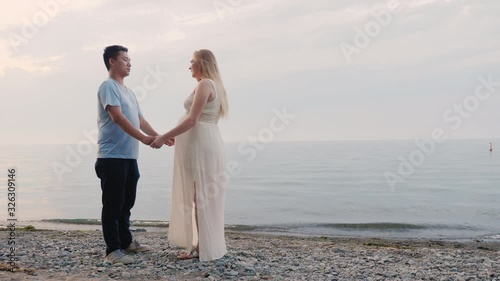 A young multi-ethnic couple stands on the seashore, a pregnant woman and an Asian man photo