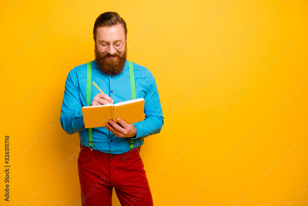 Photo of attractive guy holding writing notes in personal planner have creative idea for new project wear bright blue shirt green suspenders red pants isolated yellow color background Photo of attractive guy holding writing notes in personal planner have creative idea for new project wear bright blue shirt green suspenders red pants isolated yellow color background