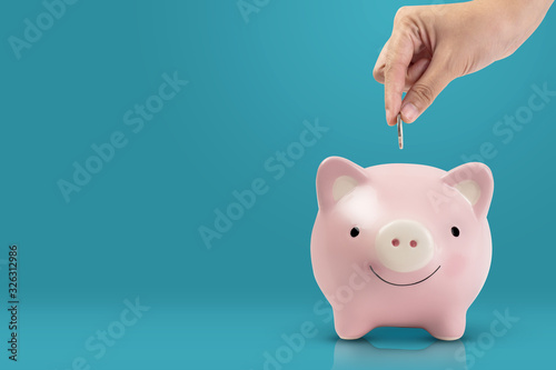 women hand putting coin into pink piggy bank on blue background