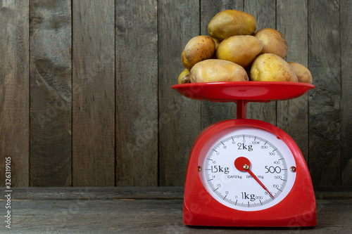 Potatoes on red scales on old wooden background.