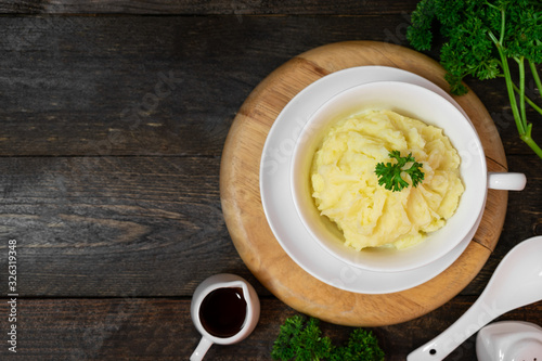 Mashed potatoes in white bowl or glass with parsley on wooden table.