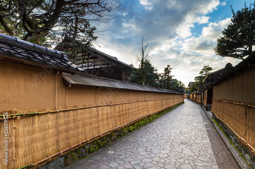 Nagamashi district or samurai district street over a dramatic sky showing the earthen walls, tsuchi-kabe, covered in winter with straw mats, Ishikawa prefecture, Japan. photo