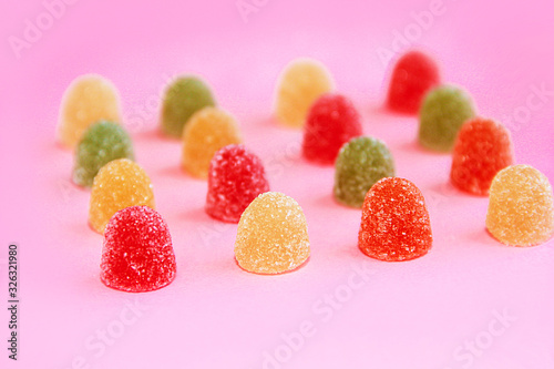 round sweet multi-colored candy marmalade in sugar sprinkles on pink background
