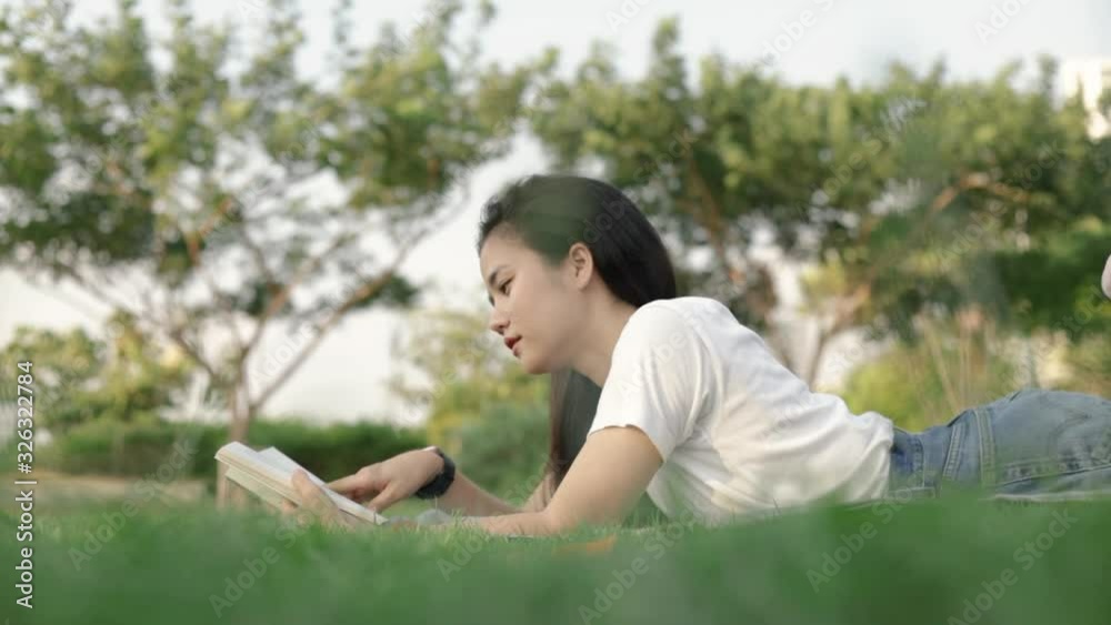 Attractive Asian woman relaxed reading a book while lying on the floor grass outdoors at a public park on the beautiful sunset. Attractive Asian woman relaxed reading a book while lying on the floor grass outdoors at a public park on the beautiful sunset.