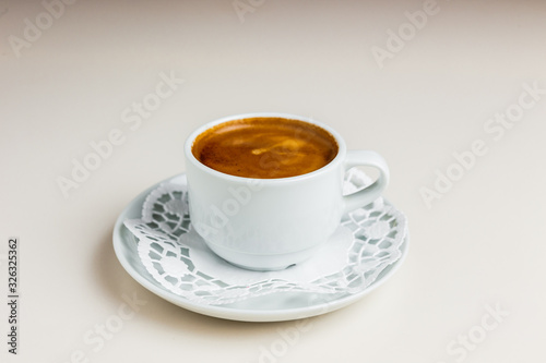 A small white cup of espresso coffee with crema on a white saucer and paper napkin