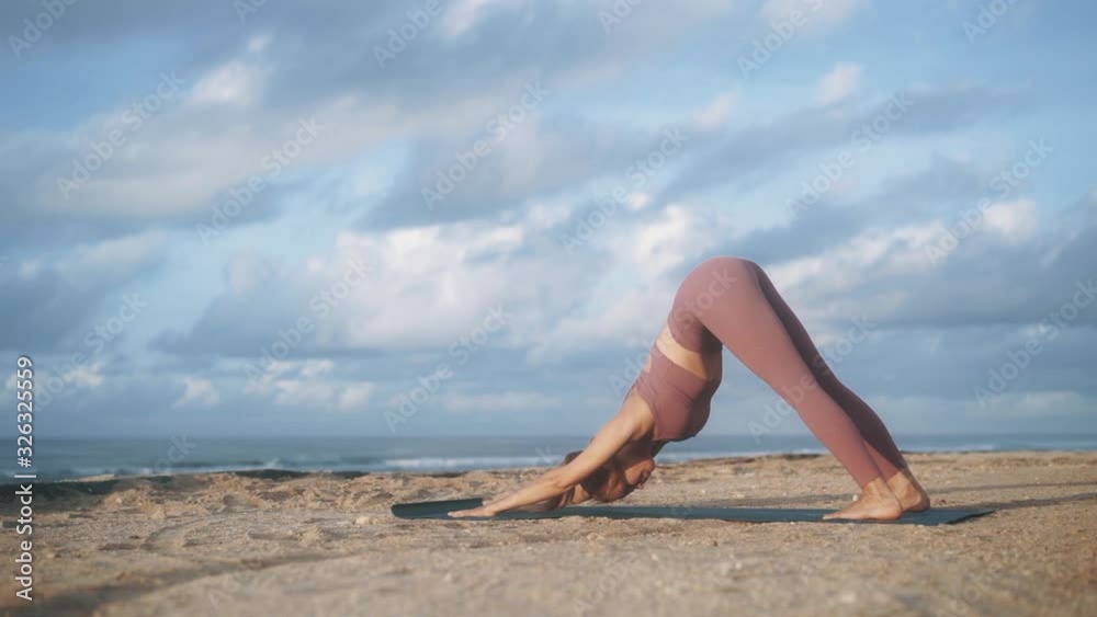Woman does yoga exercises, stretches at morning with view on ocean, slow motion